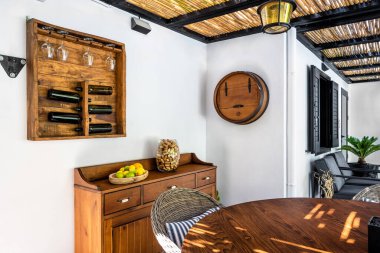 Beyaz duvarında şarap şişesi ve cam tahta tutacağı olan açık hava şarap köşesi, dolapta şarap orkları olan meyve ve vazo, yuvarlak masanın bir parçası. Seçici odak