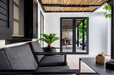 Açık hava terası koyu gri ve beyaz renklerde. Koltuklar, saksı, küçük masa ve deco ile donatılmış bir yer. Seçici odak.