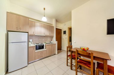 Açık sarı bej renkte basit bir mutfak tasarımı örneği. Mutfak, frigde, fırın, üç elektrikli halka, kahve makinesi, lavabo, ahşap masa adn sandalyeleri içerir..