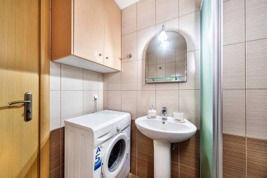 Kahverengi ve açık gri renkli standart modern banyo. Köşesinde cam duş kabini var. Lavabo, dolap, duvarda ayna..