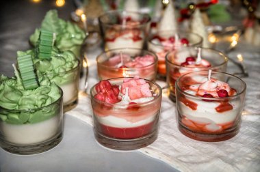 Noel tatlılarını andıran cam bardaklardaki şenlikli dekoratif mumlar, tatil masasında parlayan sıcak mum ışığı, rahat kış havası, Noel kutlaması için sezonluk dekorasyon ve yeni yıl atmosferi.