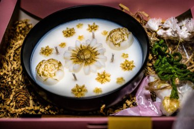 Lüks el yapımı mum hediye kutusu, beyaz balmumu, altın çiçek dekoru, birden fazla fitil, zarif kompozisyon, şenlikli estetik, özel ev dekorasyonu, tatil hediyesi konsepti, yakın plan natürmort hayat.