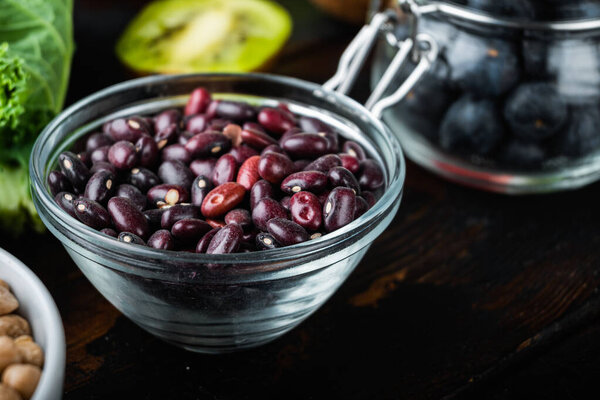 Red beans in bowl with healthy food on dark wooden background.