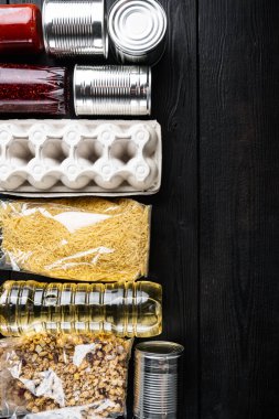 Çeşitli konserve yiyecekler ve çiğ tahıllar, market ürünleri, teslimat veya bağış, düz uzanış yazılı, siyah ahşap masa üzerinde
