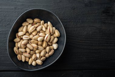 Kabuklu, tuzsuz şam fıstığı, siyah ahşap masa üzerinde, düzlük ve metin için boşluk.