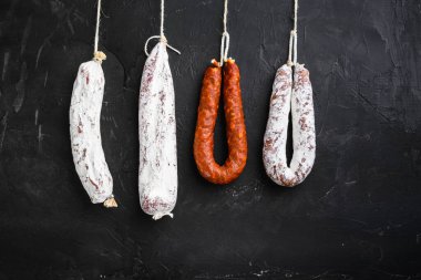 İspanyol salamı, longaniza ve sucuklu sosisler siyah desenli arka planda asılı duruyor..
