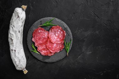 Kuru, bütün ve dilimler siyah arkaplanda salchichon sosisi, fotokopi alanı ile üst görünüm.