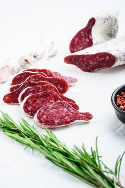 Dilimlenmiş longaniza, kurutulmuş İspanyol sosisi beyaz yüzeyde otlar ve baharatlarla..