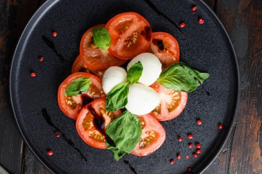 Caprese salatası domates ve fesleğen yapraklı mozzarella dilimleri zeytin ağacı koyu masa üstü manzaralı..