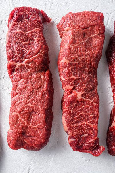 Rawset of denver steak for BBQ  cut organic meat cut top view close up over white concrete background vertical