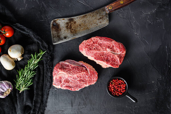 Raw  top blade cut organic meat with vegetable rosemary and other ingredients for bbq or gtrill top view over black stone background .