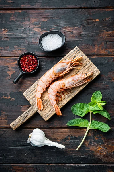 Tiger king prawns on cutting board with spices and herbs over dark rustic wooden background, flat lay, food photo.