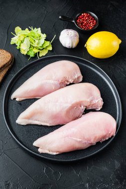 Çiğ tavuk filetosu, malzemeli, siyah arka planda.