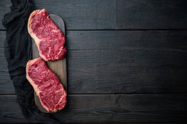 Strip fileto biftek, çiğ mermer et, siyah ahşap masa, üst görünüm, metin için fotokopi alanı