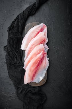 Tilapia balığı fileto eti, siyah arka planda, üst görünümde.