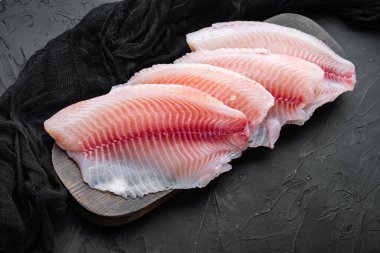 Çiğ tilapia balığı fileto eti, siyah arka planda.