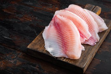 Beyaz tilapia balığı filetosu koyu ahşap arka planda kesilmiş.