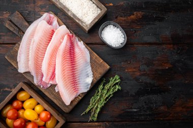 Çiğ beyaz tilapia balığı, basmati pilavı ve kiraz domatesli malzeme, koyu ahşap zemin üzerinde, metin için fotokopi alanı ile üst görünüm