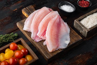 Çiğ beyaz tilapia balığı, basmati pilavı ve kiraz domatesli koyu ahşap arka planda.