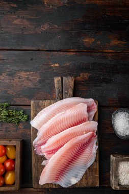 Çiğ beyaz tilapia balığı, basmati pilavı ve kiraz domatesli malzeme, koyu ahşap zemin üzerinde, metin için fotokopi alanı ile üst görünüm