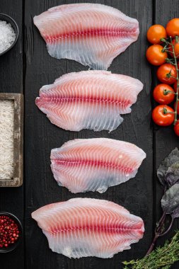 Çiğ beyaz tilapia balığı, basmati pilavı ve kiraz domatesli, siyah ahşap arka planda, üst manzara.