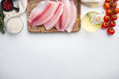 Çiğ beyaz tilapia balığı, basmati pilavı ve kiraz domatesli malzemeler, beyaz arka planda, metin için fotokopi alanı ile üst manzara