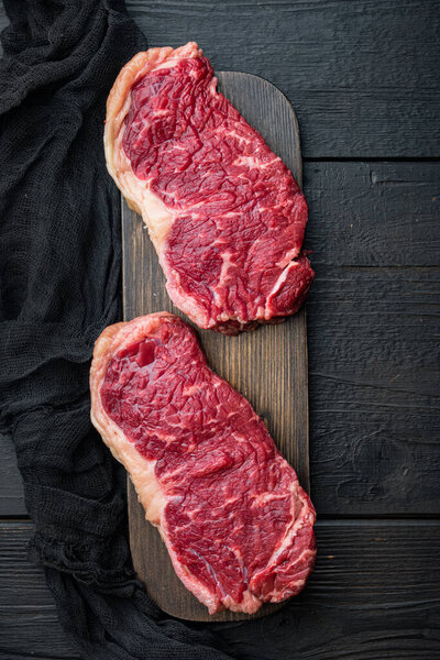 Short loin raw beef steak cut, on black wooden background, top view