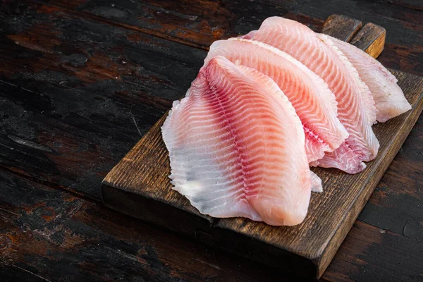 Beyaz tilapia balığı filetosu koyu ahşap arka planda kesilmiş.