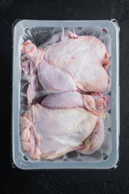Siyah zemin üzerinde çiğ tavuk seti olan plastik kap, üst görünüm.