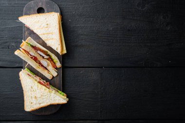 Jambonlu, peynirli, domatesli sandviç, marul, tavuk eti ve kızarmış ekmek, siyah ahşap masa üzerinde, metin için fotokopi alanı ile üst manzara