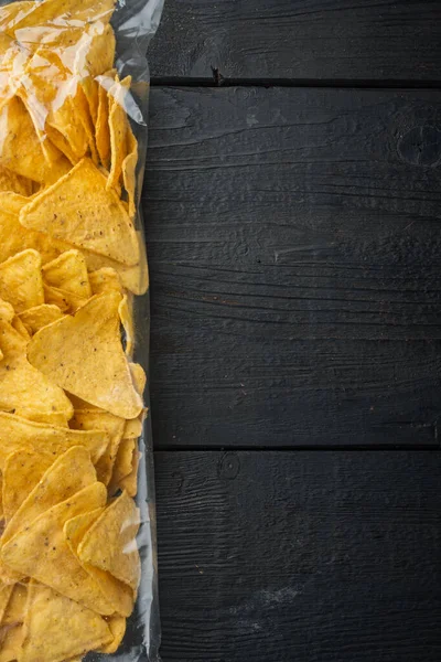 Nachos, corn tortilla in bag, on black wooden background, top view or flat lay with copy space for text
