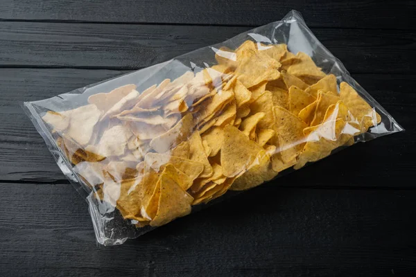 Packed and seasoned nachos and snack pack, on black wooden background