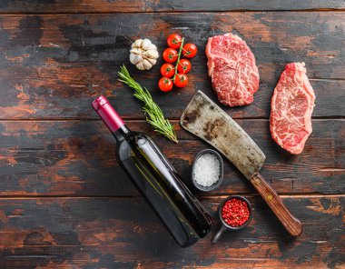 Çiğ bıçaklı biftekler baharatlı otlar ve kırmızı şarap şişesinin yanında kasap bıçağı eski, ahşap masa üstü manzaralı, metin için yer.
