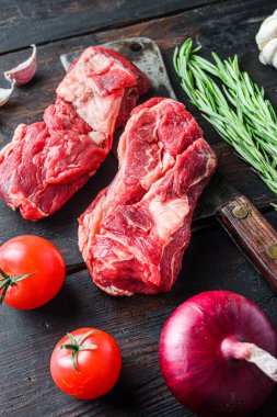 Eski kasap satırı üzerine organik çiğ Chuck bifteği, kırmızı biberiye, sarımsaklı biber ve domatesler eski, siyah ahşap masa üzerinde. Yan görünüm