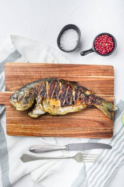 Izgara deniz kepeği ya da Dorado çiğ balığı doğrama tahtasındaki malzemelerle dokulu beyaz arka plan, üst görünüm
