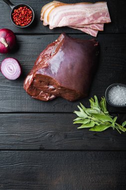 Domuz pastırmalı çiğ ciğer ve siyah ahşap arka planda soğan..