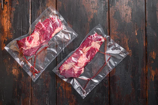 Vacuum packed Chuck roll  beef steak on dark old wooden background, top view with space for text.