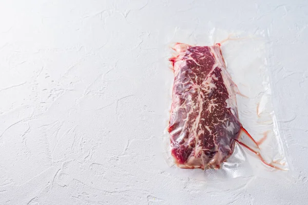 Top blade beef steak,  vacuum packed organic meat for sous vide cooking  on white concrete  textured background, top view with space for text