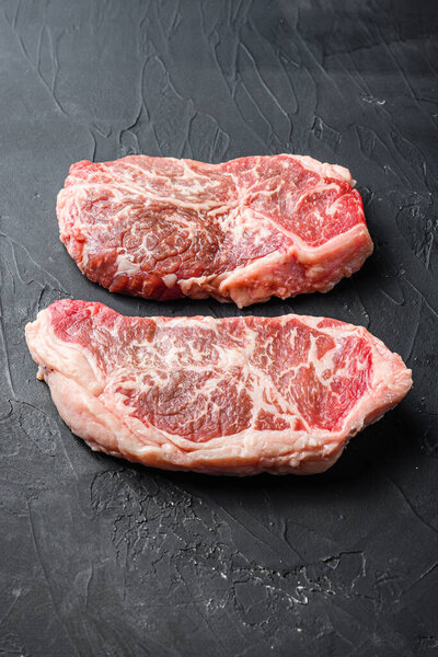 Raw top blade steak cuts, on black textured background side view