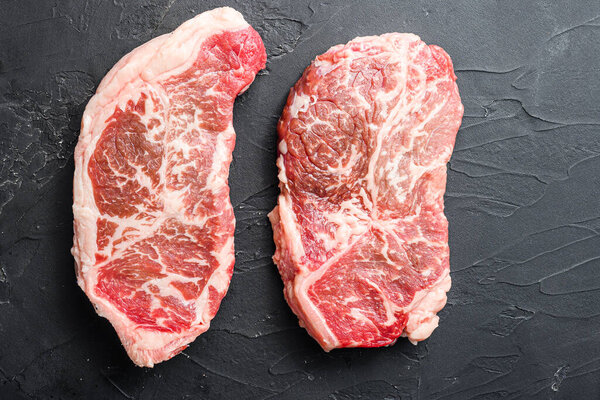 Organic top blade steak cuts, on black textured background top view