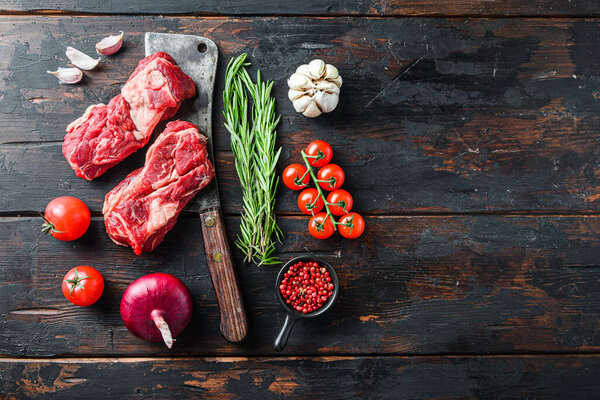 Organic raw chuck eye roll beef steak cut  with rosemary red onin, garlic peppercorns and tomatoes on old dark wooden table. Top view with space for text