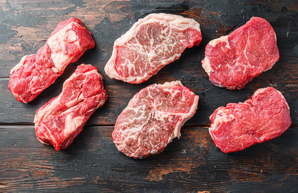 Variety of fresh Black Angus Prime raw beef steakes on old rustic dark wooden background, top view