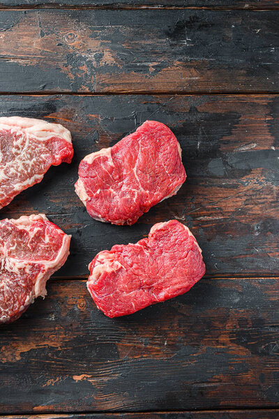 Variety of organic raw beef steakes rump cut  on old rustic dark wooden background, top view with space for text.