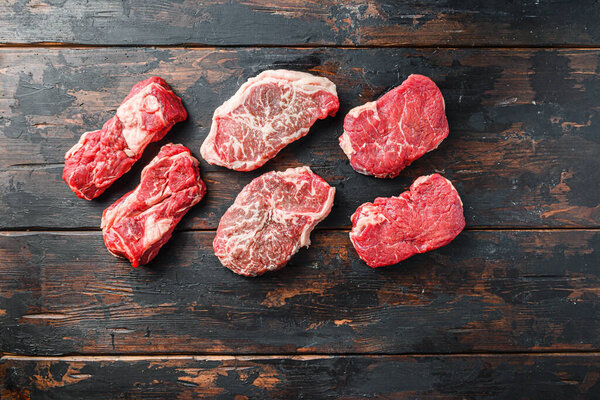 Variety of organic raw beef steakes rump, chuck roll and top blade  cut  on old rustic dark wooden background, top view with space for text