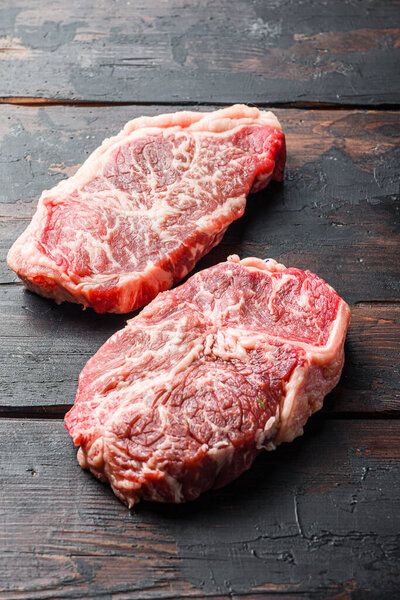 Raw marbled beef steak, top blade organic meat cut. On dark wooden background, side view