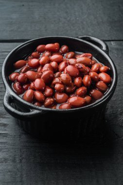 Kırmızı fasulye konservesi, siyah ahşap masa arkasında.