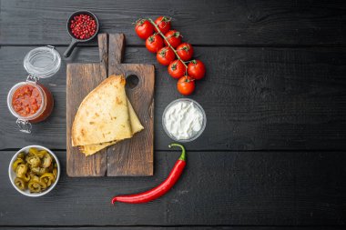 Baharatlı quesadilla soslu ve otlu tortilla, siyah ahşap masa arkaplanı, üst görünüm düz metin alanı için fotokopi alanı ile yatıyordu