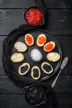 Canapes with black sturgeon, and salmon fish caviar, on black wooden table background, top view flat lay