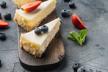 Gri arka planda çilekli, yaban mersinli ve naneli cheesecake.