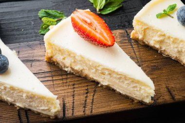 Klasik New York Cheesecake dilimleri, siyah ahşap masa arkasında.
